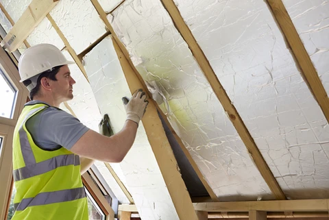 Ouvrier en équipement de sécurité installant de l'isolation thermique entre chevrons de toiture dans combles en construction