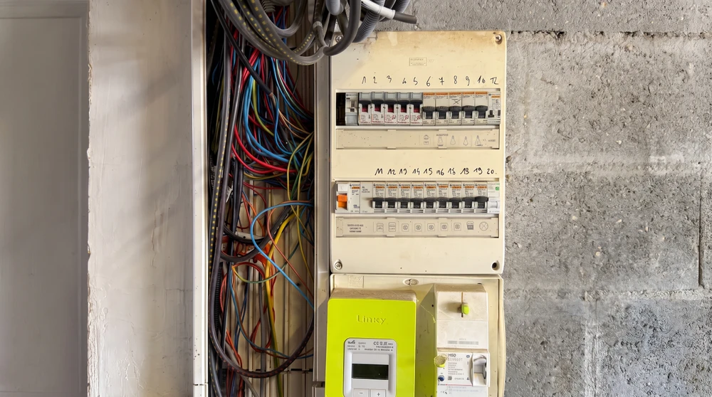 Tableau électrique résidentiel français encastré, composé de deux rangées de disjoncteurs modulaires (12 circuits), un différentiel 30mA, câblage multicolore apparent (rouge, bleu, jaune, vert, noir)