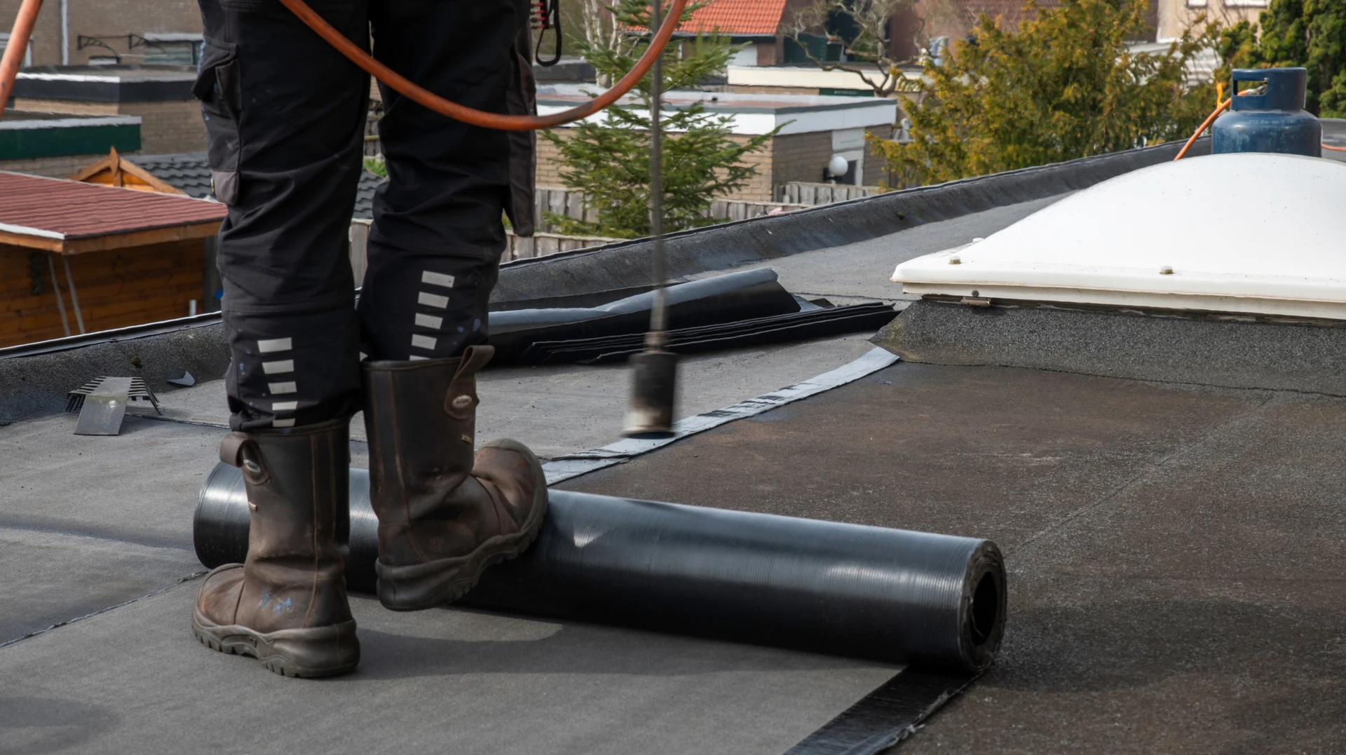Ouvrier appliquant un revêtement d'étanchéité liquide sur une toiture-terrasse en béton à l'aide d'un rouleau à manche télescopique bleu