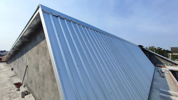 Détail photographique en gros plan d'une toiture pendant des travaux d'étanchéité, montrant l'application ou la pose d'une membrane d'étanchéité (bitumineuse ou synthétique) sur la pente d'une toiture. Matériau gris, noir ou blanc clairement visible, fixation mécanique ou collage en cours. Surface de la toiture légèrement mouillée ou humide, suggérant les conditions d'un environnement extérieur. Mains d'un ouvrier qualifié en gants de travail manipulant ou lissant le matériau. Environnement de jour naturel, éclairage rasant soulignant les détails de texture. Cadrage professionnel et technique mettant l'accent sur la qualité et la rigueur du travail d'étanchéification, sans texte ni logo visible.